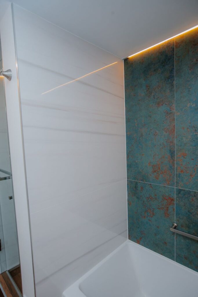 Large format white wall tile meeting blue green feature tile above acrylic bathtub in renovated master bathroom