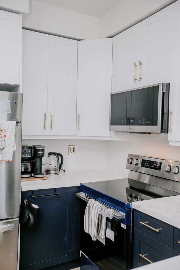 Navy blue shaker lower cabinets and white upper cabinets with glass inserts, white quartz countertop and gold faucet