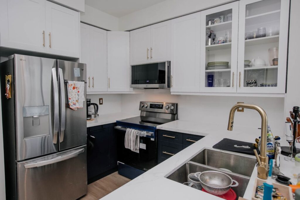 Renovated condo kitchen with LG refrigerator, white shaker upper cabinets, navy base cabinets and white quartz countertop