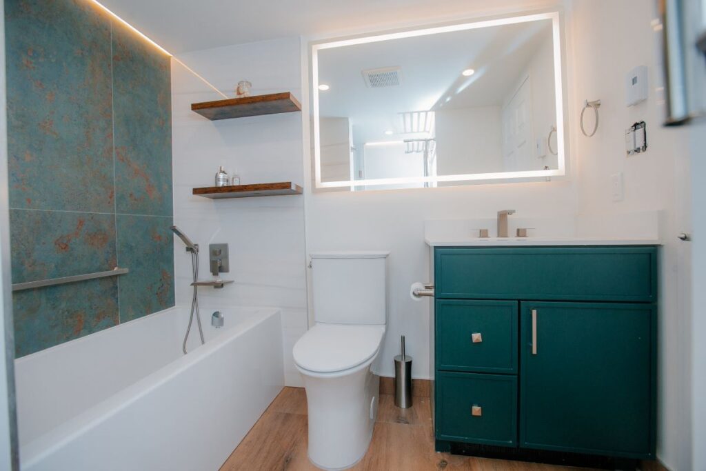 Renovated master bathroom with dark green vanity, bathtub, toilet, and LED mirror