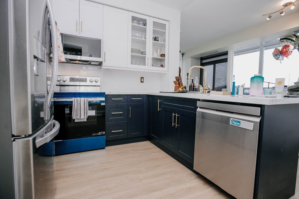 Two tone kitchen renovation with navy lower cabinets, white glass front uppers, stainless dishwasher and gold gooseneck faucet