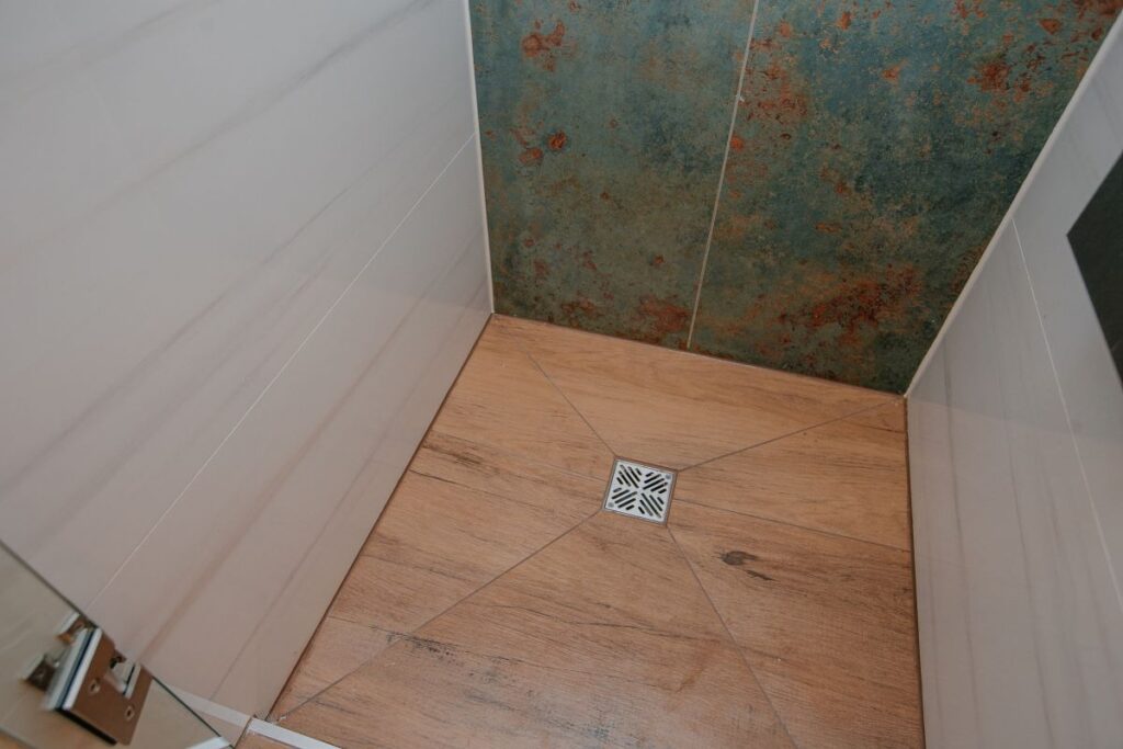 Wide view of acrylic bathtub, blue green feature wall, floating wood shelves, and glass shower enclosure