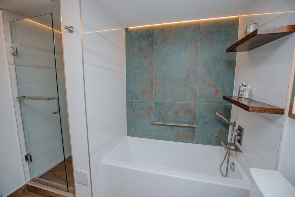 Wide view of bathtub, floating shelves, and glass shower enclosure