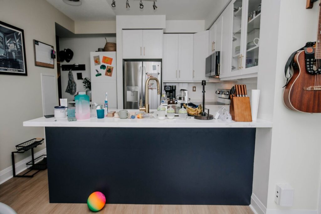 Wide view of renovated condo kitchen from living area showing navy peninsula, white shaker cabinets and LG French door refrigerator