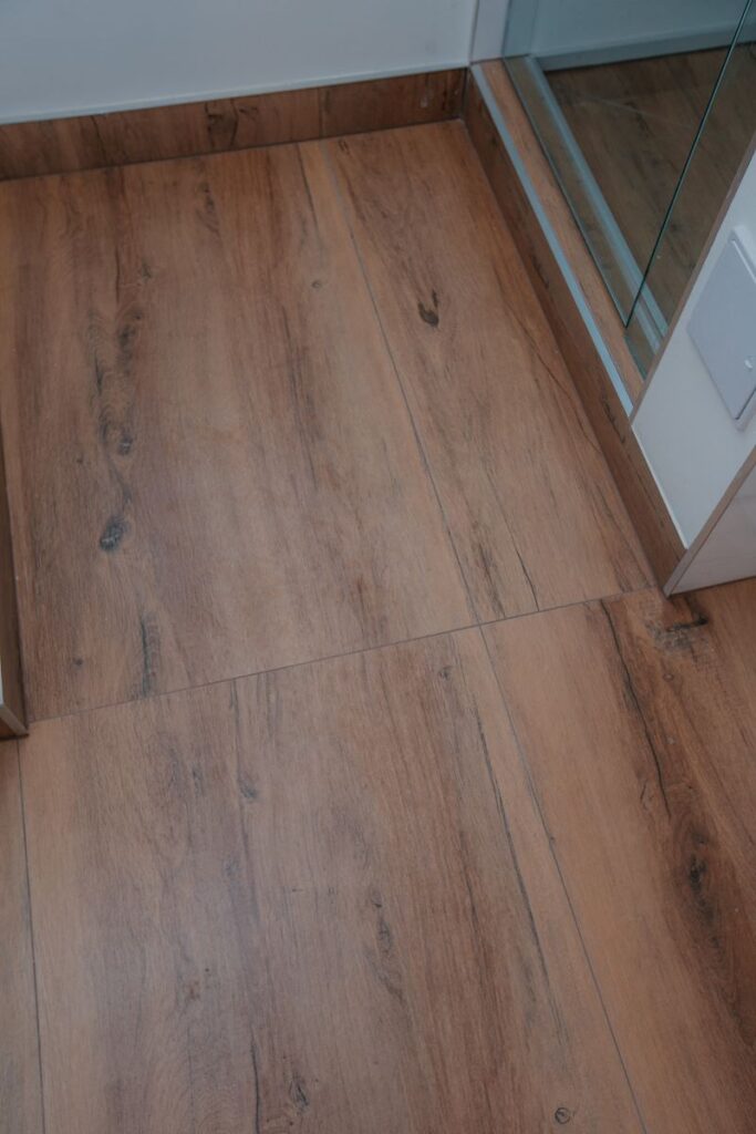 Wood look porcelain floor tile near glass shower enclosure in renovated master bathroom
