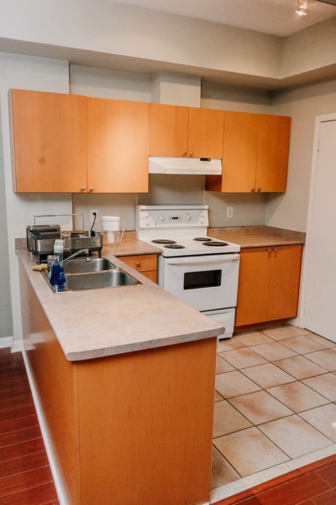 before condo kitchen renovation with peninsula, orange cabinets, white stove and ceramic tile floor in downtown Toronto