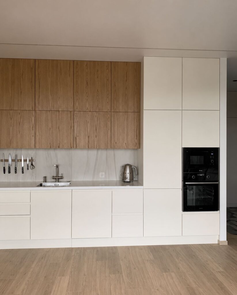 Minimalist kitchen renovation with wood upper cabinets, white base cabinets, marble backsplash, and stainless steel SMEG kettle