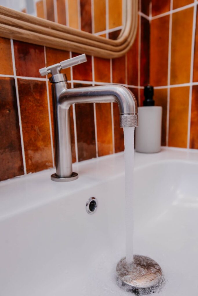 Modern bathroom faucet detail on floating vanity with rust tile backsplash
