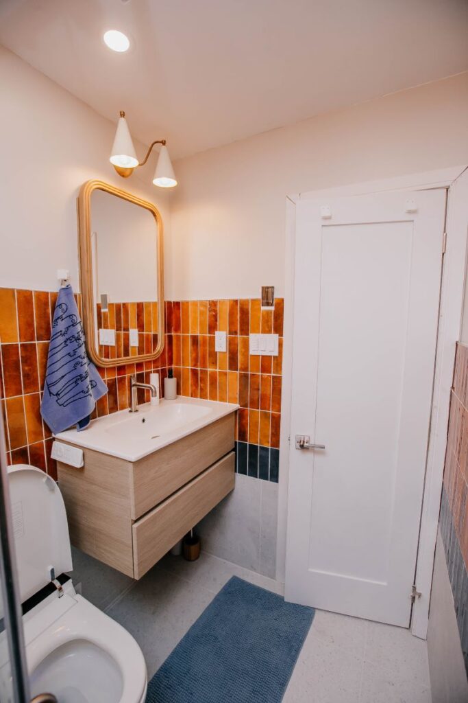 Modern compact bathroom with bold rust tile, floating vanity and curved wood framed mirror