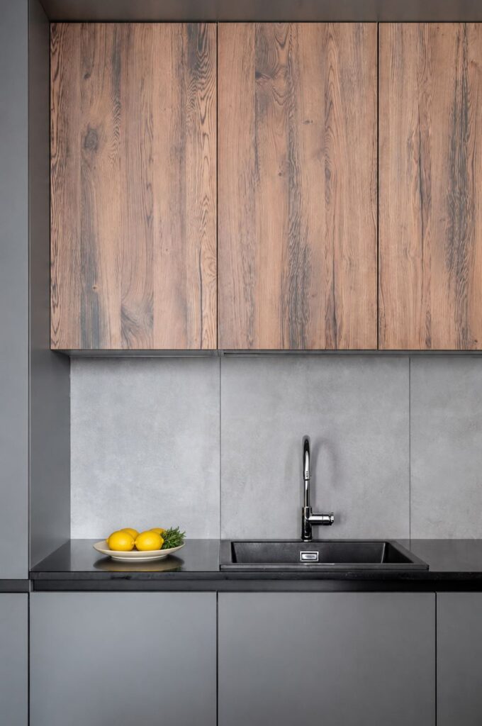 Modern kitchen renovation in Toronto with wood upper cabinets, grey backsplash, black countertop, and lemons on a ceramic plate