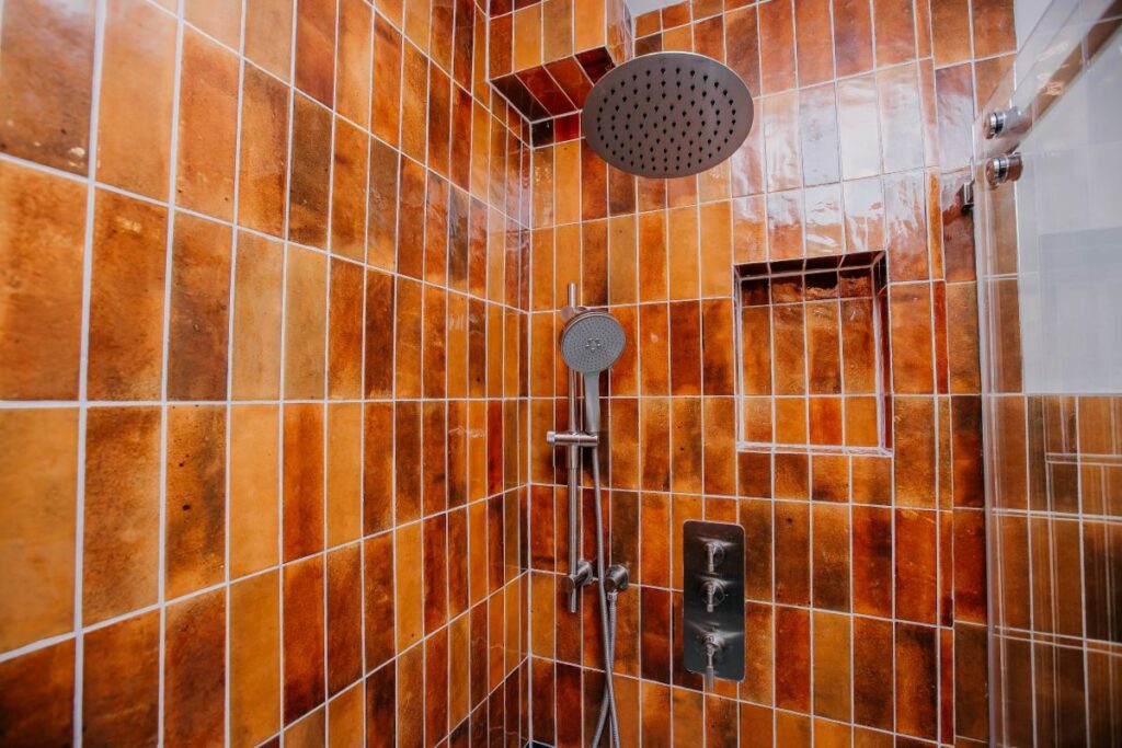 Modern shower system with rain head and handheld on rust toned glossy wall tile