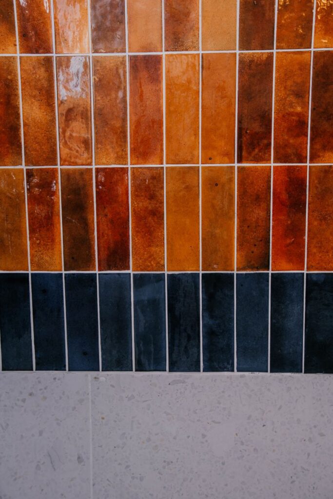 Rust glossy wall tile with dark accent band and terrazzo look lower tile detail