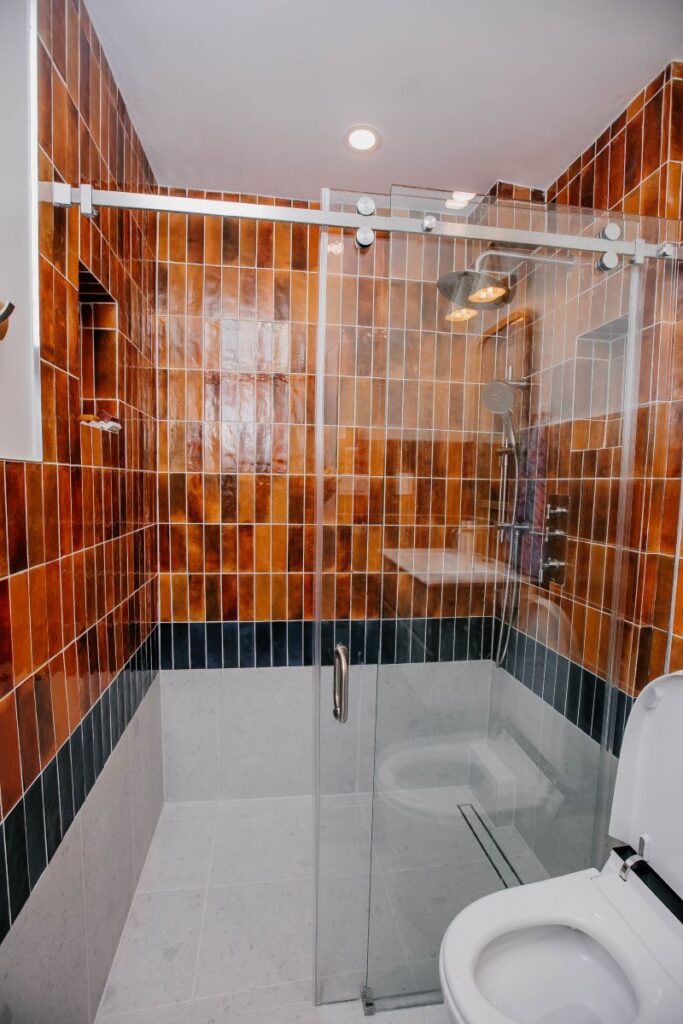 Tub to shower bathroom remodel with rust wall tile, sliding glass enclosure and curbless shower