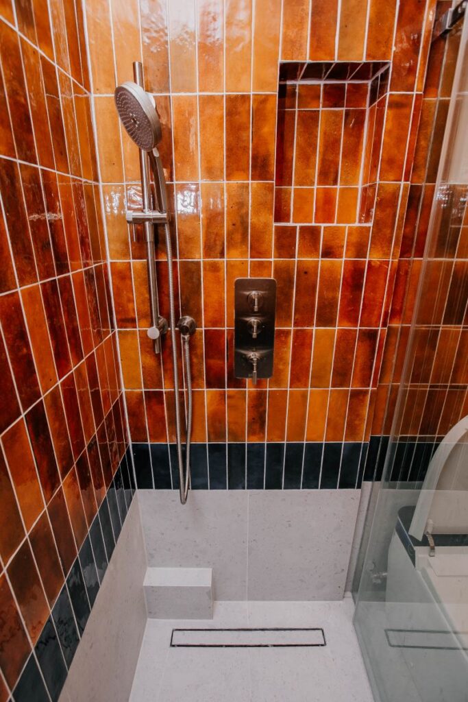 Walk in shower with custom niche, dark accent tile band and modern shower fixture