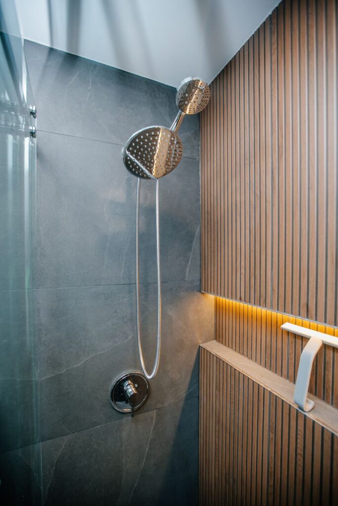 Chrome shower system on grey porcelain with a backlit oak slat wall, recessed shelf and squeegee