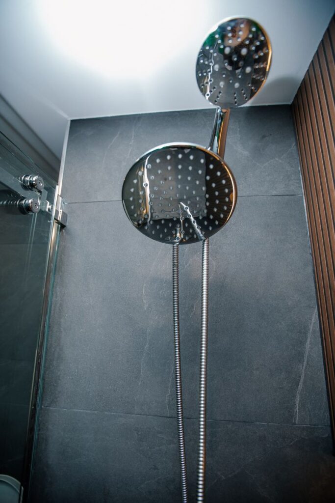 Close up of a chrome dual rain and handheld shower head against large format grey porcelain tile