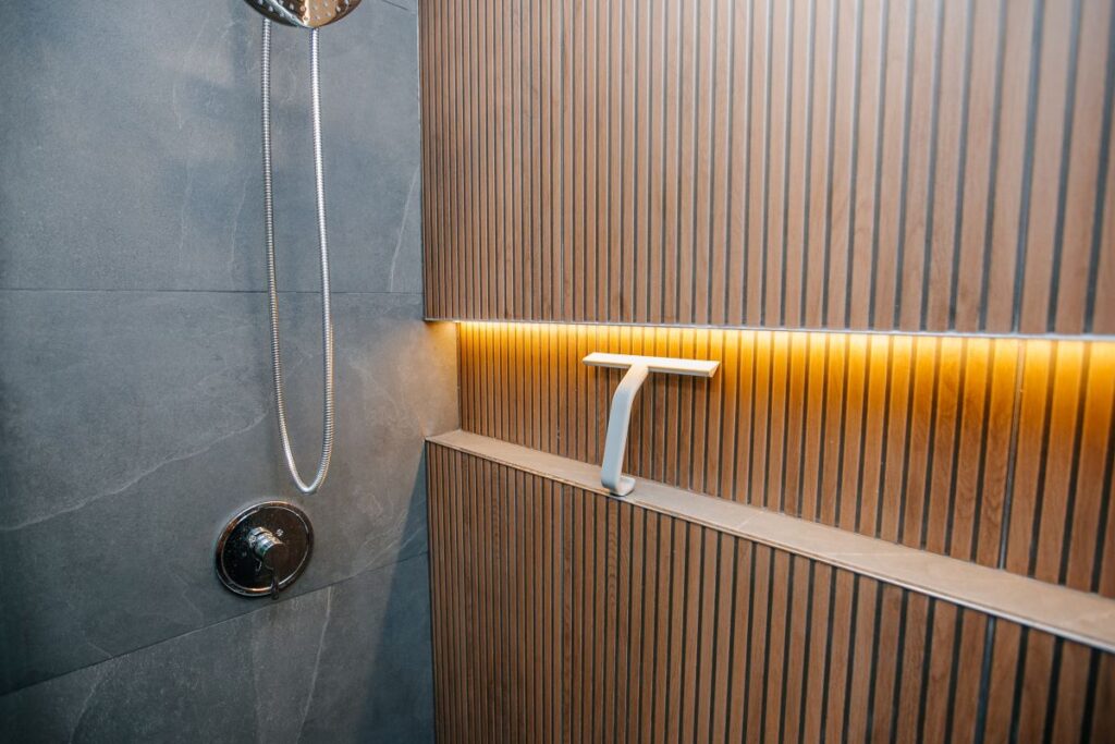 Detail of a chrome pressure balance shower valve and a backlit oak slat shelf with warm LED glow