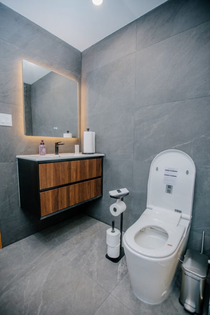 Floating black and walnut vanity with integrated basin, black faucet, LED mirror and a smart toilet on grey stone look porcelain