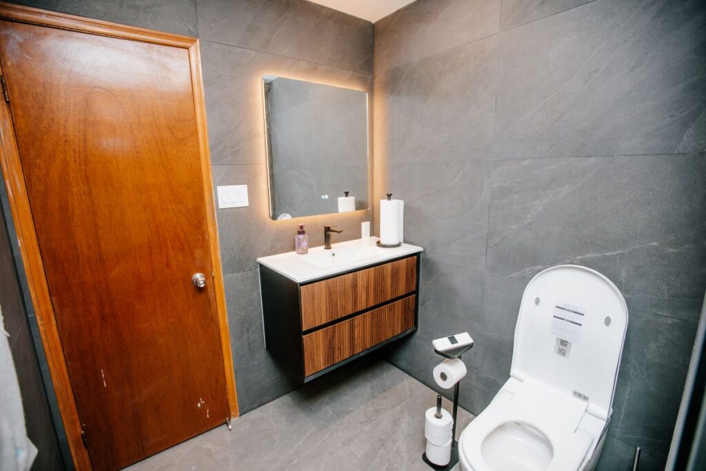 Modern bathroom vanity wall with LED mirror, fluted walnut floating cabinet and a smart bidet toilet beside a wood door