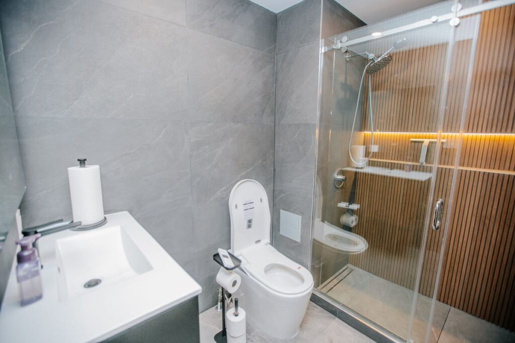 Renovated bathroom with a white vanity basin, smart toilet and a glass walk in shower with an oak slat accent wall