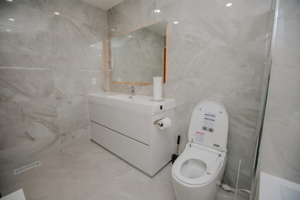 Renovated bathroom with pearl marble walls and glass shower panel in North York