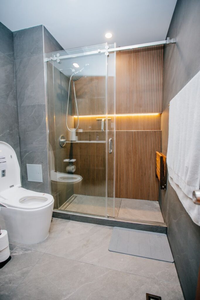 Tub to shower conversion with a sliding glass walk in shower, backlit oak slat wall, folding bench and smart toilet
