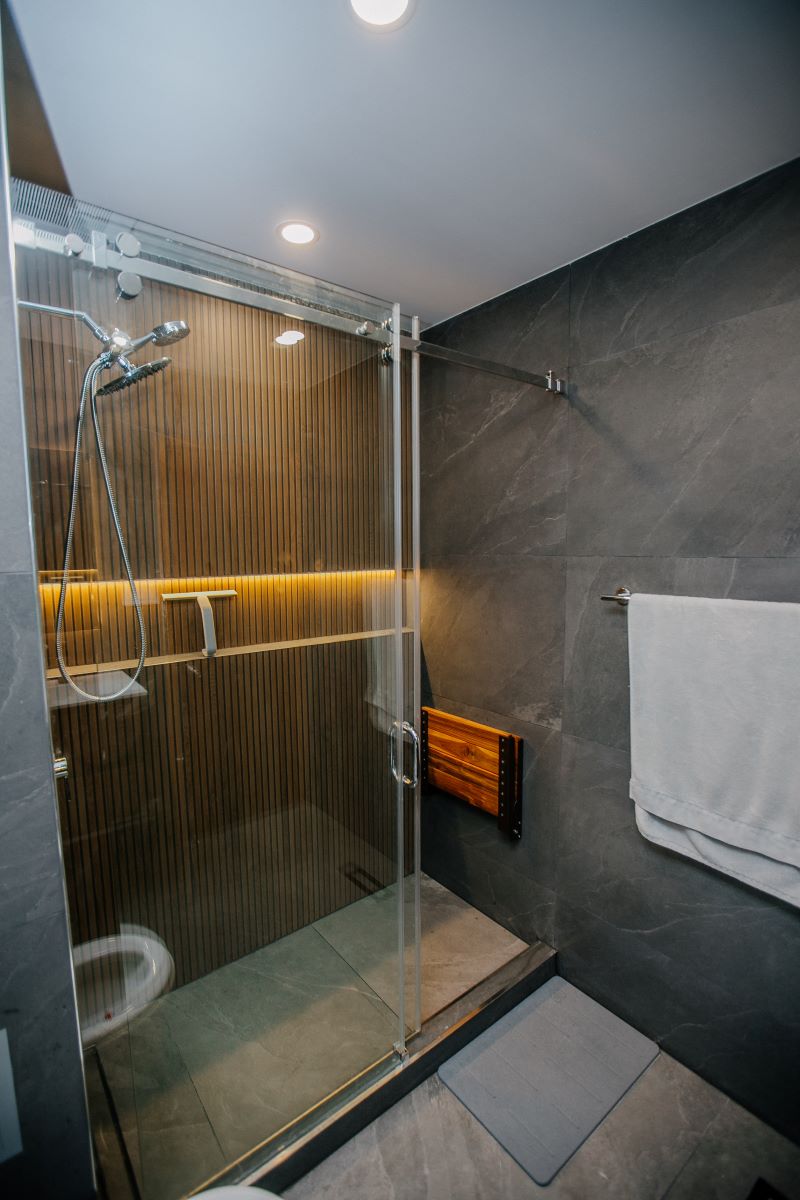 Walk in shower with sliding glass door, oak slat feature wall with backlit LED shelf and grey porcelain tile