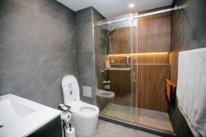 Wide view of a completed tub to shower conversion with smart toilet, floating vanity and a backlit oak slat shower wall
